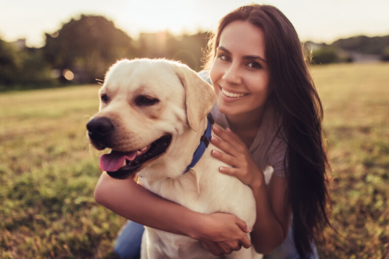Attractive young woman with labrador outdoors. Woman on a green grass with dog labrador retriever. Smiling and looking at the camera.